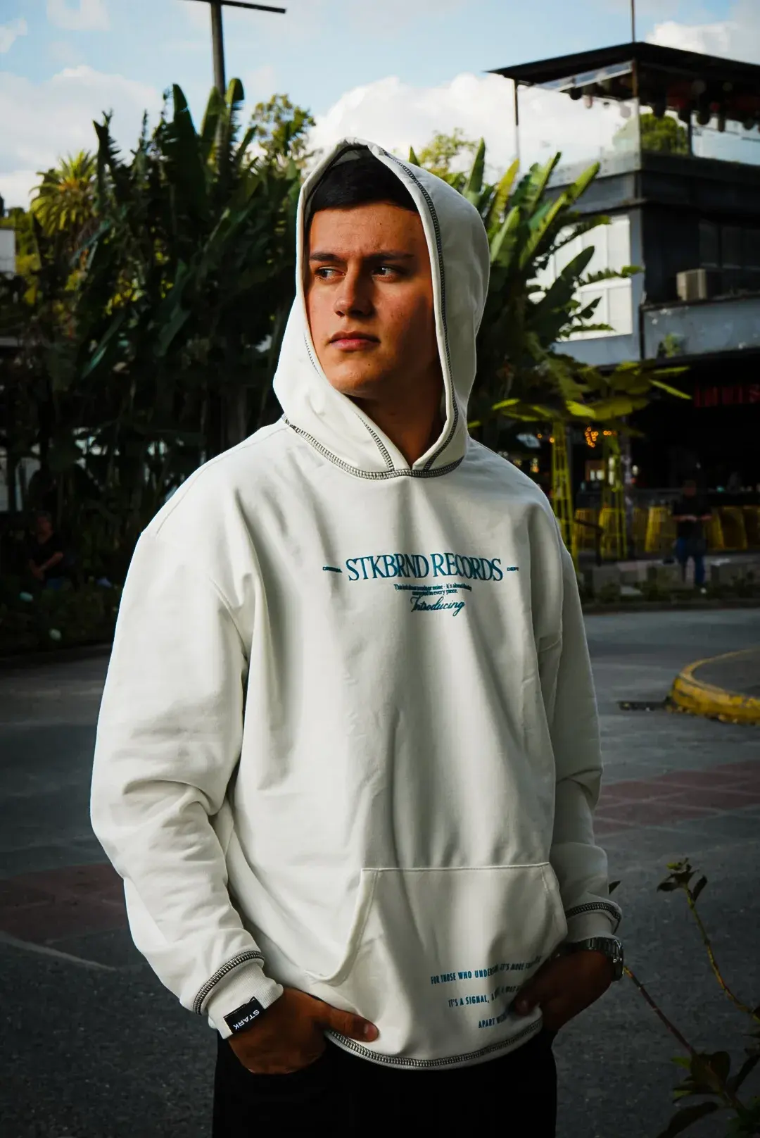 Modelo con el Buso Crudo Records y la capucha puesta, al atardecer