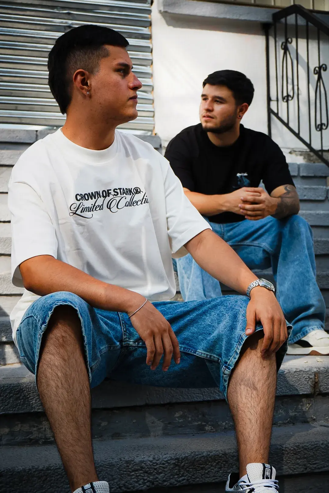 Dos modelos sentados en unas escaleras, con camisa Crown Oversize y camisa negra