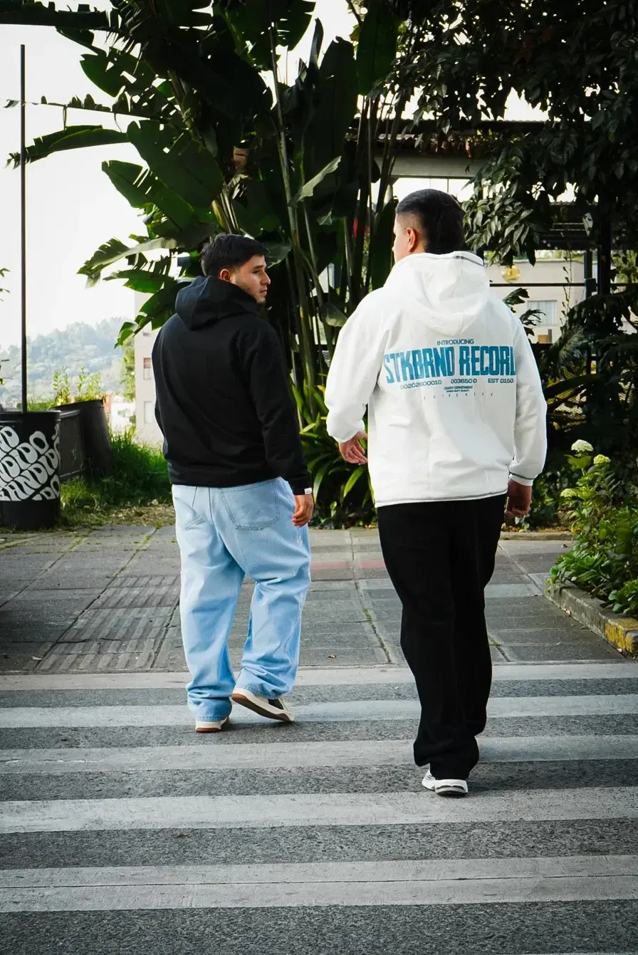 Dos modelos de espalda cruzando un paso peatonal en Manizales, con buso Crudo Records