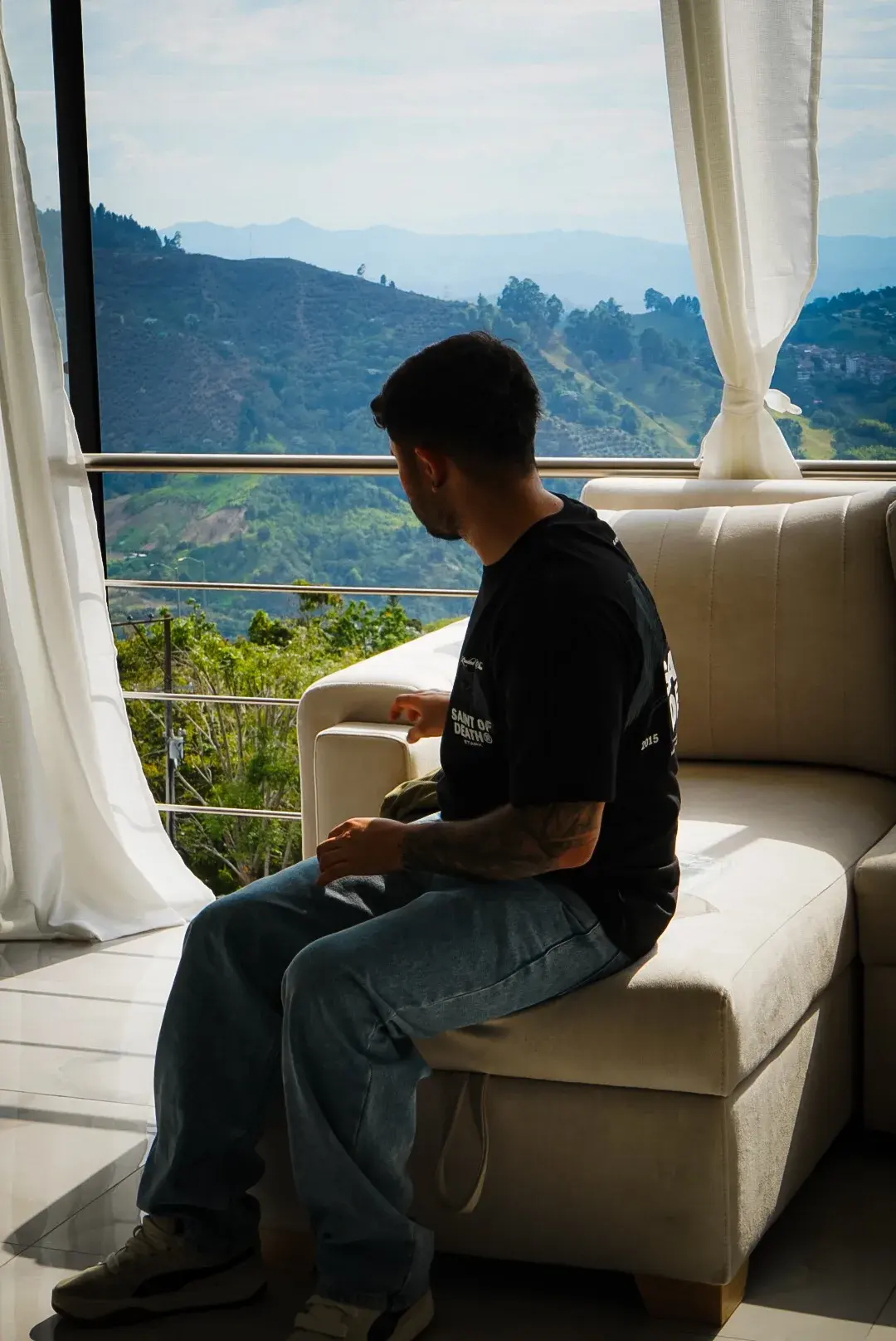 Modelo con la Camisa Saint Of Death frente a un ventanal, con las montañas de Manizales al fondo